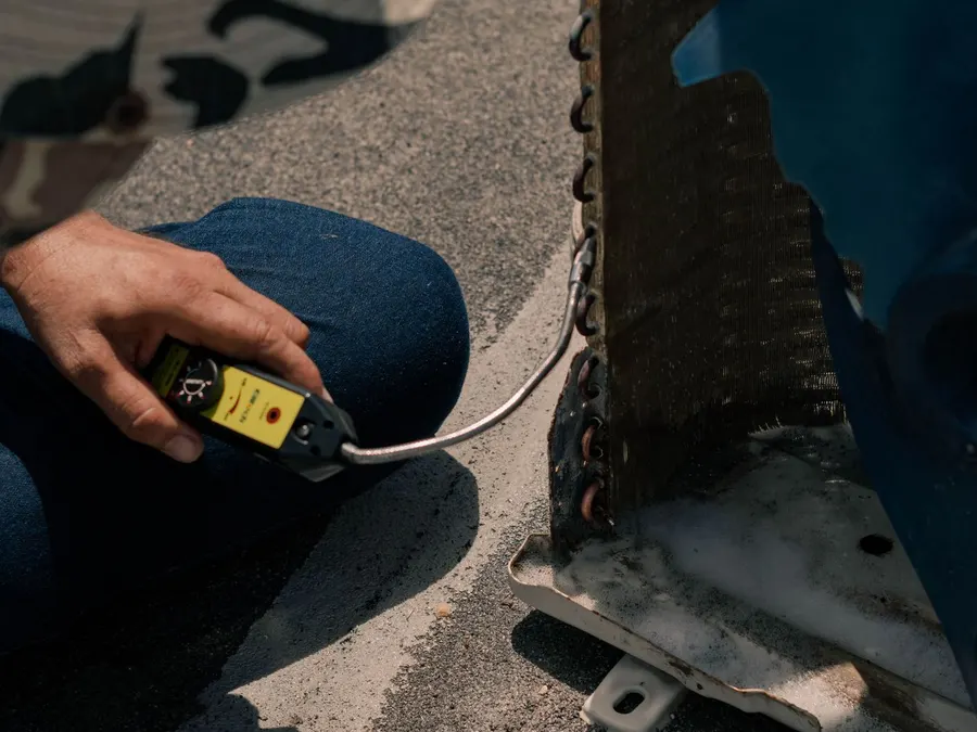 Technician using a leak detector on a heating and cooling unit coil